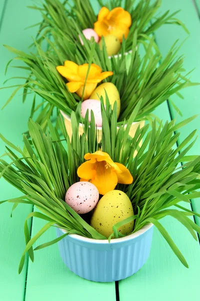 Пасхальные яйца в мисках с травой на зеленом деревянном столе вблизи — стоковое фото
