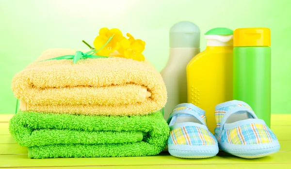 Cosméticos para bebés, toallas y botas sobre mesa de madera, sobre fondo verde —  Fotos de Stock