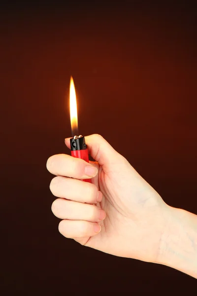 Acendedor em chamas na mão feminina, no fundo marrom escuro — Fotografia de Stock