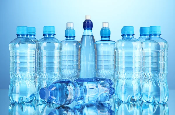 Různé lahve s vodou na modrém pozadí — Stock fotografie