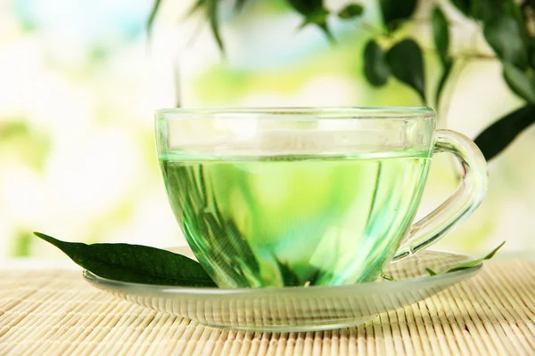 बांबू चटईवर हिरव्या चहाचा पारदर्शक कप, निसर्ग पार्श्वभूमीवर — स्टॉक फोटो, इमेज