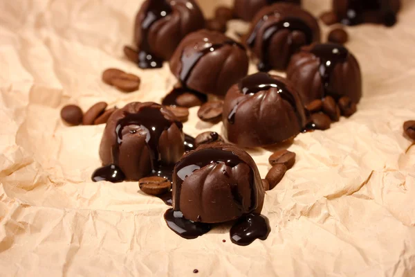 Шоколадні цукерки та кавові зерна на фоні бежевого паперу — стокове фото