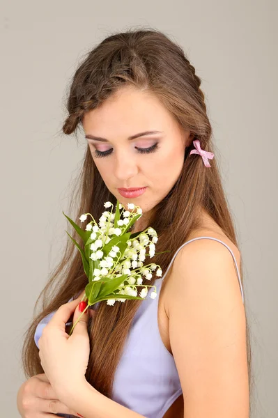 Giovane donna con bella acconciatura e fiori, su sfondo grigio — Foto Stock