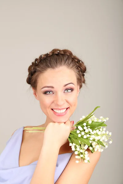 Молода жінка з красивою зачіскою і квітами, на сірому фоні — стокове фото