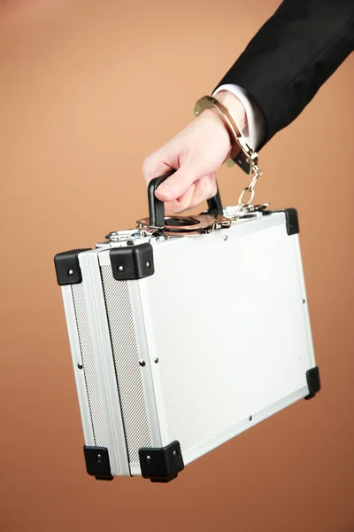 Hand with handcuff and suitcase, on color background — Stock Photo, Image