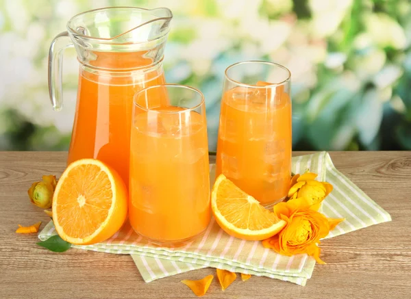 Copos e jarro de suco de laranja na mesa de madeira, no fundo verde — Fotografia de Stock