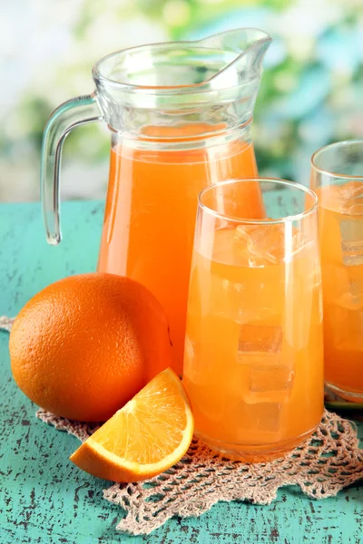 Glasögon och tillbringare med apelsinjuice på blå trä bakgrund — Stockfoto