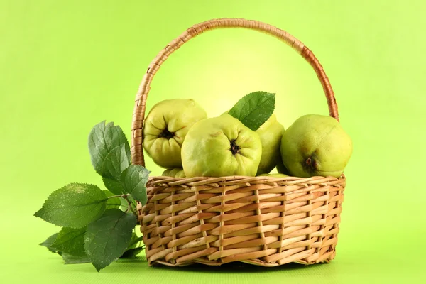 Süße Quitten mit Blättern im Korb, auf grünem Hintergrund — Stockfoto