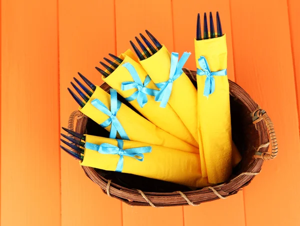 Fourchettes en plastique bleu enveloppées dans des serviettes en papier jaune, dans un panier en osier, sur fond en bois de couleur — Photo