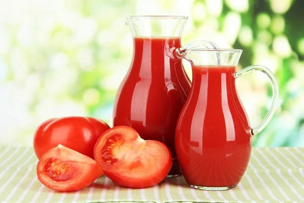 Jugo de tomate en jarras sobre mesa sobre fondo brillante —  Fotos de Stock