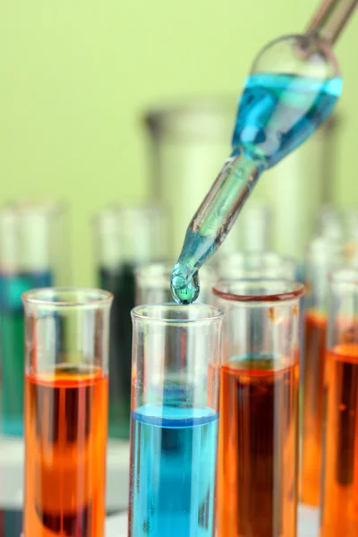 Pipeta de laboratório com gota de líquido de cor sobre tubos de ensaio de vidro, de perto — Fotografia de Stock