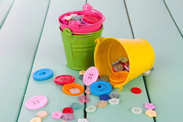 Colorful buttons strewn from buckets on wooden background — Stock Photo, Image