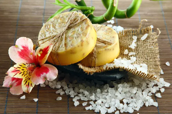 Hand-made soap and sea salt on grey bamboo mat — Stock Photo, Image