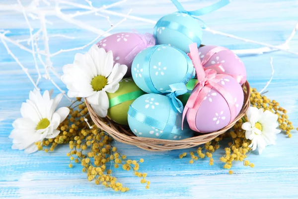 Easter eggs in basket and mimosa flowers, on blue wooden background — Stock Photo, Image