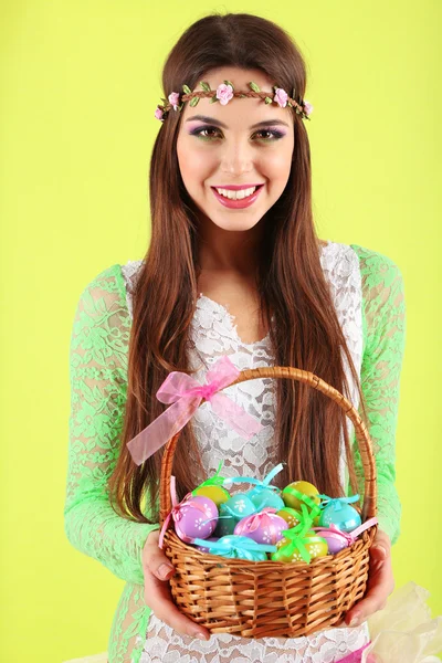 Happy female holding basket with Easter eggs, on green background — Stock Photo, Image
