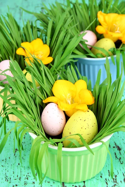 Påskägg i skålar med gräs på gröna träbord närbild — Stockfoto