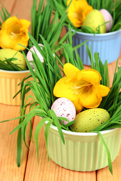 Easter eggs in bowls with grass on wooden table close up