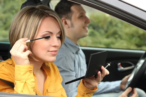Portrait of young beautiful couple sitting in the car (woman applying makeup) — Stock Photo, Image
