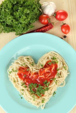 Cooked spaghetti carefully arranged in heart shape and topped with tomato sauce, on wooden background