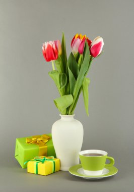 Hediyeler ve gri arka plan üzerinde çay ile kova güzel laleler