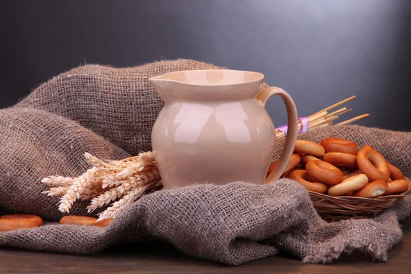 Pot van melk, smakelijke bagels en spikelets op houten tafel, op grijze achtergrond — Stockfoto