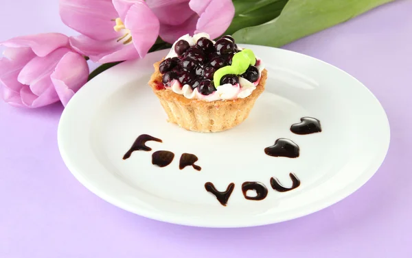 Sweet cake with blackberry and chocolate sauce on plate, on color background — Stock Photo, Image