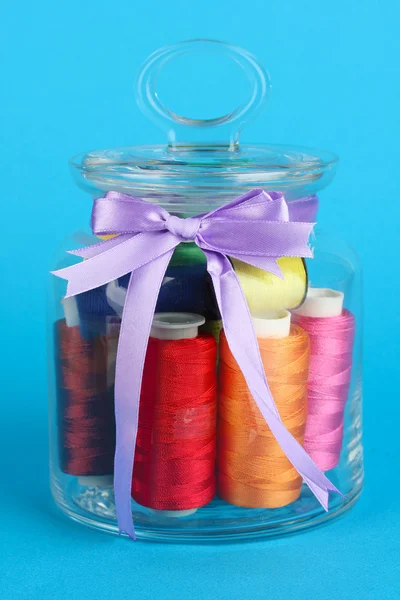 Glass jar containing various colored thread on blue background — Stock Photo, Image