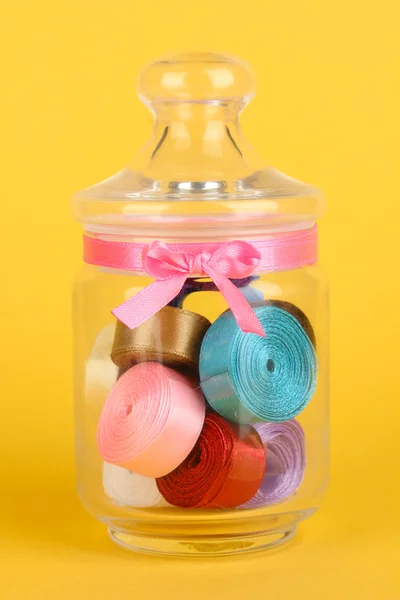 Tarro de vidrio que contiene varias cintas de colores sobre fondo amarillo — Foto de Stock