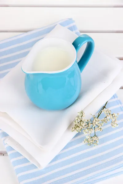 Blue jug with milk on napkin on wooden picnic table close-up — Stock Photo, Image