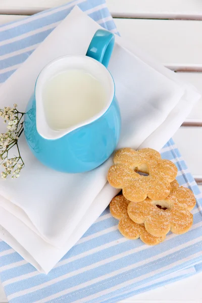 Blue jug with milk and cookies on wooden picnic table close-up — Stock Photo, Image