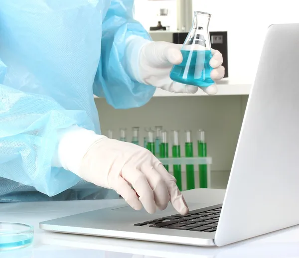 Scientist entering data on laptop computer with test tube close up — Stock Photo, Image