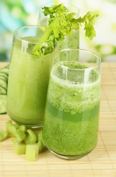 Glasses of green celery juice on bamboo mat, on green background — Stock Photo, Image