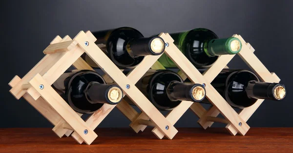 Ahşap stand gri arka plan üzerine yerleştirilen şarap şişeleri — Stok fotoğraf