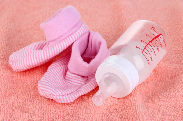 Bottle for milk and booties on pink towel background — Stock Photo, Image