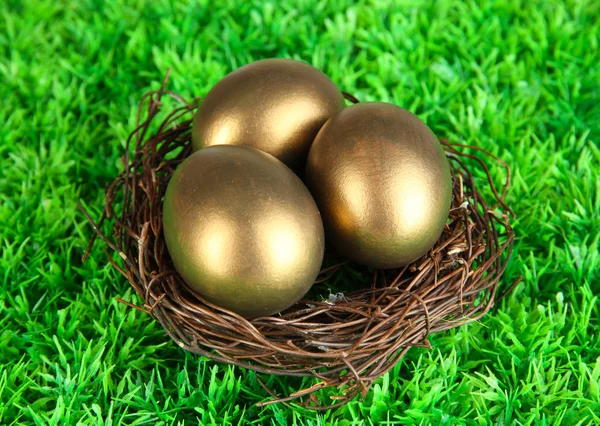 Three golden eggs in nest on grass — Stock Photo, Image