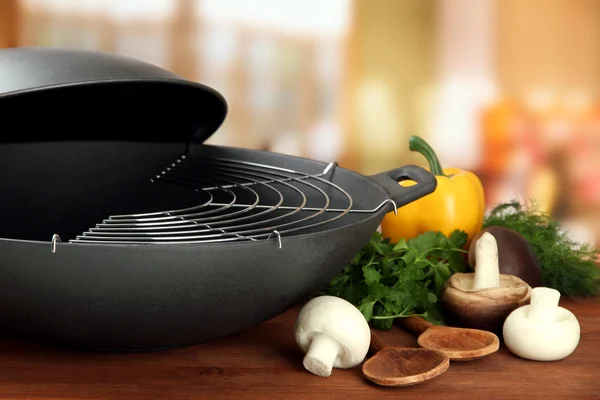 Black wok pan and vegetables on kitchen wooden table, close up — Stock Photo, Image