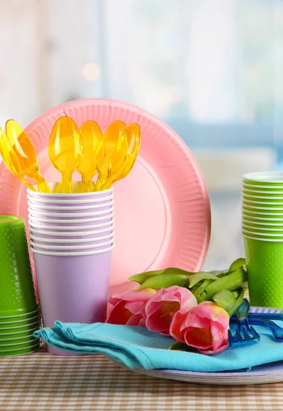 Multicolored plastic tableware on table with tulips close up — Stock Photo, Image