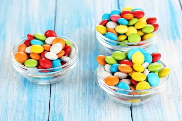 Coloridos caramelos en cuencos de vidrio sobre fondo de madera azul —  Fotos de Stock