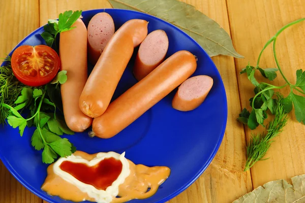 Sausage, greens, tomato on plate on wooden table — Stock Photo, Image