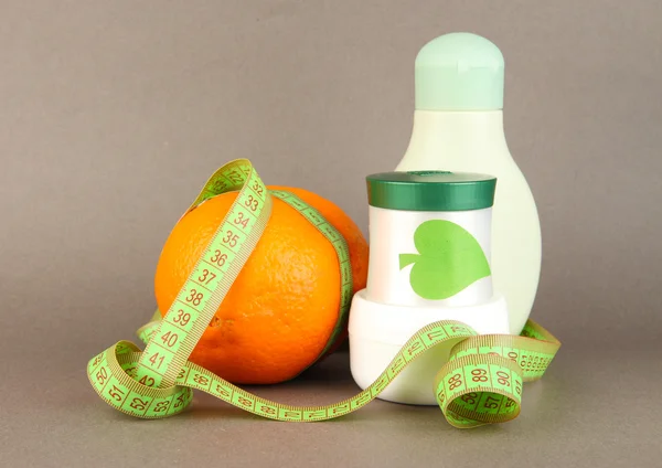 Orange with measuring tape and body cream, on color background — Stock Photo, Image