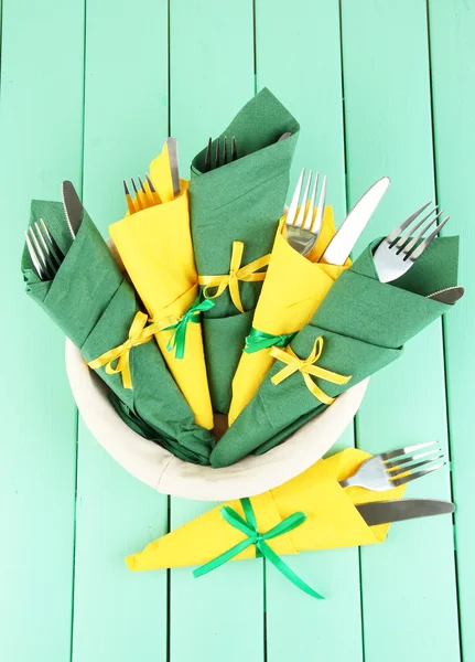 Forchette e coltelli avvolti in tovaglioli di carta verde e giallo, su sfondo di legno a colori — Foto Stock