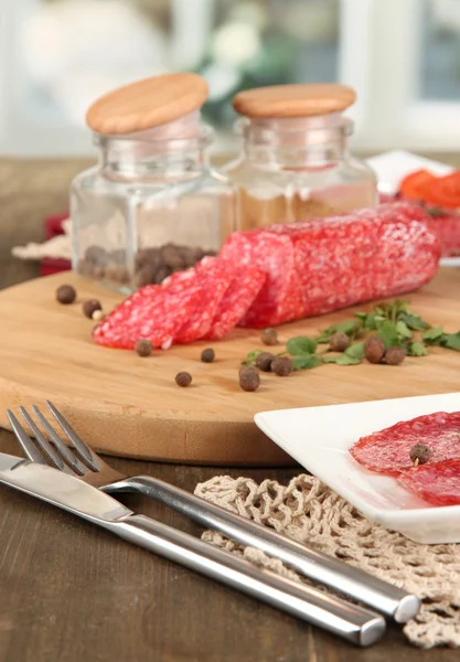 Smaczne salami na płytkę i wyżywienie na drewnianym stole na tle okna — Zdjęcie stockowe