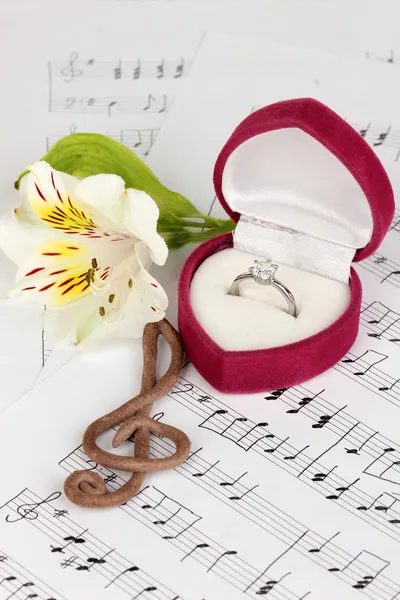 Treble clef, bloem en box bedrijf trouwring op muzikale achtergrond — Stockfoto