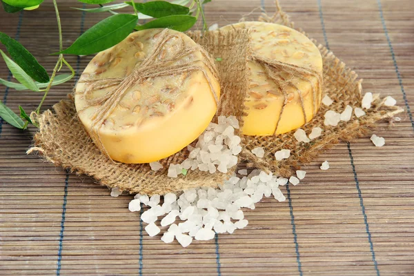 Hand-made soap and sea salt on grey bamboo mat — Stock Photo, Image