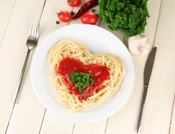 Gotowane spaghetti starannie ułożone w kształcie serca i polane sosem pomidorowym, na tle drewniane — Zdjęcie stockowe