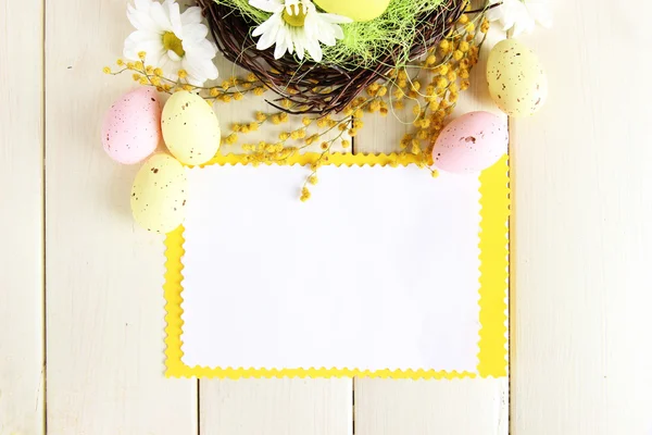 Порожня листівка з великодніми яйцями та квітами мімози на білому дерев'яному фоні — стокове фото