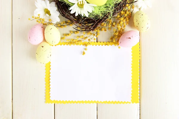 Carta vuota con uova di Pasqua e fiori di mimosa, su fondo di legno bianco — Foto Stock