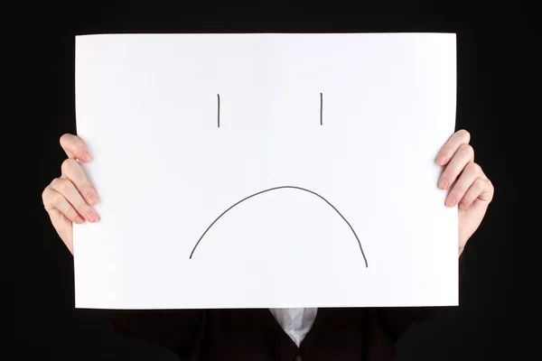 Woman holding paper with sad emoticon, isolated on black — Stock Photo, Image