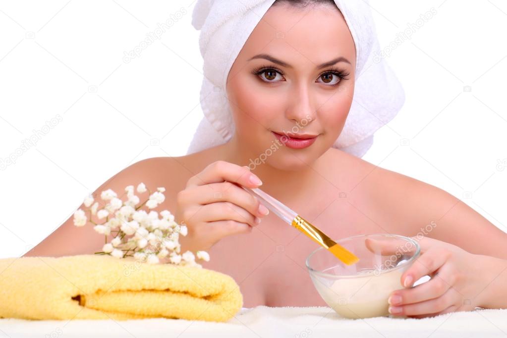 Beautiful young woman with cream for face mask and towel on her head isolated on white