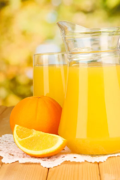 Vaso lleno y jarra de jugo de naranja y naranjas en mesa de madera al aire libre —  Fotos de Stock